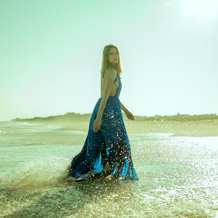 Caucasian female model in flowy blue gown walking through ocean wave photographed by Marty Gottlieb